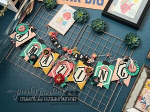 Close-up of a completed 'YOU ARE AMAZING' banner with colorful die-cut letters and embellishments hanging on a wall.