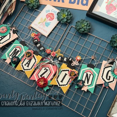 Close-up of a completed 'YOU ARE AMAZING' banner with colorful die-cut letters and embellishments hanging on a wall.